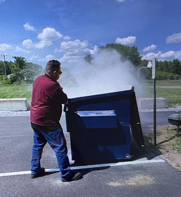 Image of a man putting using a fire extinguisher to put out a smoking dumpster fire